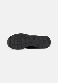 Fekete sneaker talpa texturált, mintás felülettel és logóval. Barázdákkal és kiemelkedő részekkel rendelkezik a tapadás és a stabilitás érdekében.