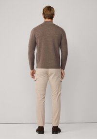 Hnedý pletený sveter s okrúhlym výstrihom, skombinovaný so svetlo béžovými cargo nohavicami s bočnými vreckami, nosený s tmavými čižmami.