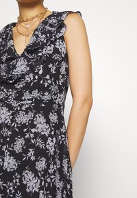 Black floral dress features a ruffled neckline, short sleeves, and pockets. It has a fitted bodice and flowing skirt with light gray patterns.