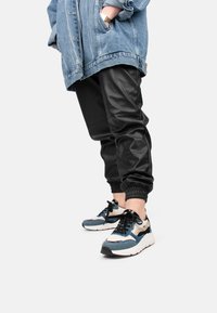 Jeansjacke mit ausgefranstem Detail, kombiniert mit schwarzen Jogginghosen aus Kunstleder und mehrfarbigen Sneakers. Besitzt elastische Bündchen und Schnürsenkel.