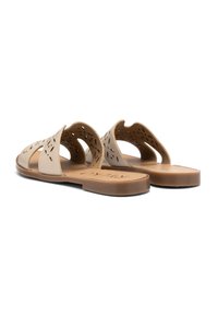 Beżowe sandały z wycięciami, odkrytymi bokami i płaską brązową podeszwą. Teksturowana cholewka posiada perforacje dla wentylacji.
