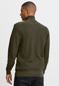 Olivgrüner Strickpullover mit hohem Kragen, gerippten Säumen und einer strukturierten Oberfläche. Hat schmal geschnittene Ärmel und einen geraden Saum.