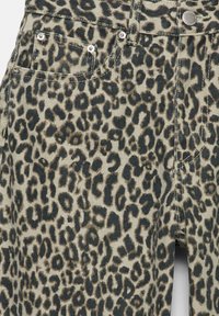 Denim material s potiskom leopardove kože ima svetlo bež podlogu sa tamnim smešnim i crnim tačkama, dopunjen metalnim dodacima i šavovima.