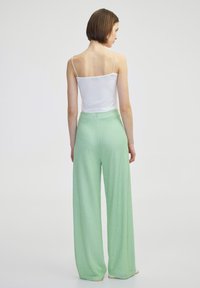 Witte spaghetti-top gecombineerd met groene textuur wijde broek, met een hoge taille en subtiel patroon, weergegeven vanaf de achterkant.