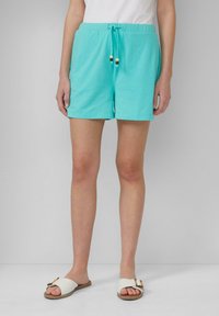 Shorts di cotone turchese con vita regolabile e dettagli in perline di legno, abbinati a sandali bianchi a ciabatta. Design semplice, lunghezza al ginocchio.