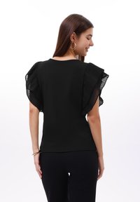 Černý top s skládacími, průhlednými volánkovými rukávy a kulatým výstřihem. Upnutý design s hladkou texturou a přímým lemem.