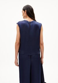 Navy blue, sleeveless top with a smooth texture. Features a keyhole back neckline with a small button closure and a relaxed fit.