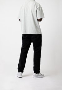 Camiseta de algodón gris de manga corta, combinada con pantalones de mezclilla negros. Zapatillas blancas visibles, con detalles grises y logo.