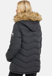 Puffet sort vinterjakke med hætte, der har faux fur-detaljer, chevronmønster og cirkulært logo-patch på venstre ærme.
