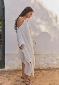 Robe légère blanche avec une coupe ample, des manches ouvertes et des bretelles ajustables. Texture lisse et ourlet asymétrique.