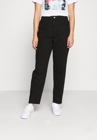 Pantalones negros de cintura alta con un diseño de pierna recta, fabricados en denim. Llevados con una camiseta gráfica y zapatillas blancas.