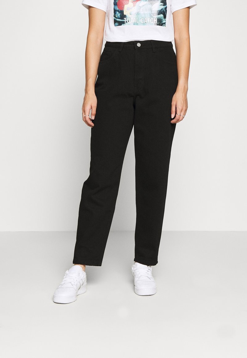 Pantalones negros de cintura alta con un diseño de pierna recta, fabricados en denim. Llevados con una camiseta gráfica y zapatillas blancas.