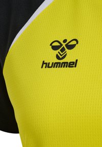 Tessuto sportivo giallo e nero con logo hummel nero raffigurante un'ape stilizzata e il nome del marchio in lettere minuscole.
