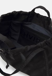 Sac fourre-tout noir à ouverture supérieure montrant une poche intérieure zippée étiquetée "HVISK" et deux anses sur fond blanc.