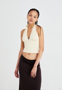 Crème haltertop met een V-hals ontwerp, lichtgewicht stof en een strakke pasvorm, gecombineerd met een donkerbruine, gedrapeerde rok.