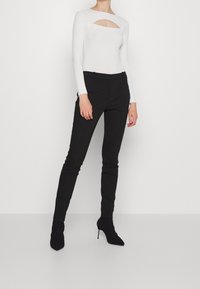 Witte geribbelde lange mouwen bodysuit met een vierkant uitsnede, gecombineerd met zwarte slim-fit broeken en zwarte hoge enkellaarsjes.