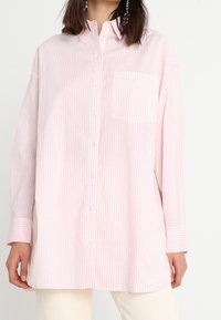 Camicia a maniche lunghe, con bottoni, di colore rosa chiaro con strisce verticali bianche, dotata di taschino sul petto e vestibilità rilassata. Tessuto in cotone.