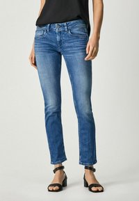 Modré denimové džíny s slim fit, mírným vyblednutím, designem pěti kapes a rovného střihu, doplněné černými sandály na kotníky.