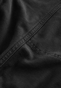 Tissu noir à texture lisse, présentant des coutures visibles le long des bords et des plis subtils, indiquant un tombé décontracté.