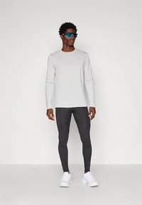 Hellgraues langärmeliges Sportshirt und schwarze Leggings, ergänzt durch sportliche, blau getönte Sonnenbrillen und weiße Turnschuhe.