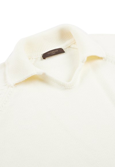 Cremfarbener Strick-Polo mit weicher Textur, ausgestattet mit einem klassischen Kragen und einem dezenten SLOWEAR-Label im Nacken.