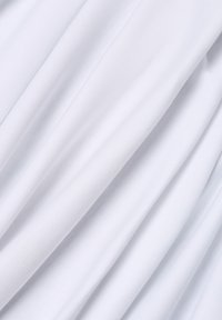 Nahaufnahme eines weichen weißen Gewebes mit diagonalen Falten und subtiler Textur, die sanfte Schatten und Highlights erzeugen.