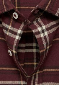 Burgundy kostkovaná košile s límečkem, s bílými a béžovými kostkovanými vzory. Dvě plastové knoflíky viditelné na výstřihu. Měkká textilie.