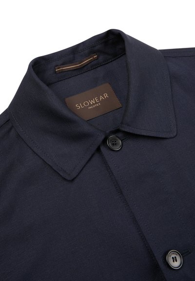 Marineblaues Hemd mit einem Button-Down-Kragen aus strukturiertem Stoff. Verfügt über ein Logetikett und einen einzelnen schwarzen Knopf am Kragen.