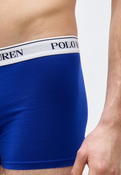 Κοντινό πλάνο ενός ατόμου που φοράει μπλε ανδρικά εσώρουχα τύπου boxer με λευκή ζώνη μέσης που φέρει το κείμενο «POLO RALPH LAUREN».