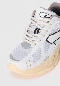 White athletic sneaker with mesh and synthetic materials, featuring a thick cream sole, silver accents, and prominent grey detailing.
