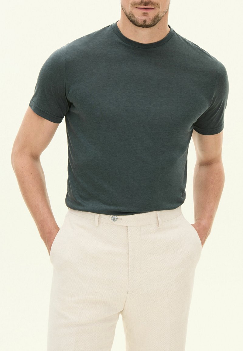 Mörkgrön kortärmad T-shirt i en figurnära stil, tillverkad av slät tyg, i kombination med ljusbeige skräddarsydda byxor med knappdetalj.