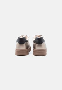 Pár béžových tenisek s hnědými podrážkami a černými patami, zobrazených zezadu na bílém pozadí.