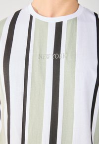 Camiseta con rayas verticales en blanco, verde y negro. Presenta el texto bordado "NEW YORK" en plateado. Fabricada en algodón, con diseño de cuello redondo.