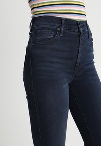 Jeans de color azul oscuro hechos de denim, con cinco bolsillos, cremallera y cierre de botón, y un ajuste slim. La tela tiene un acabado suave y un ligero estiramiento.