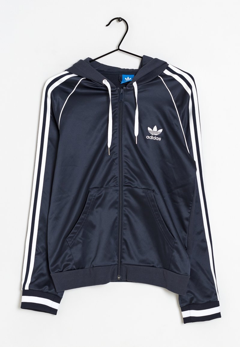 Tummansininen Adidas-huppari, jossa on vetoketju, valkoiset raidat hihoissa ja kenguru-taskut. Valmistettu sileästä kankaasta.