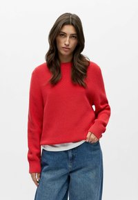 Suéter rojo de punto con textura acanalada, cuello redondo y ajuste holgado, combinado con jeans de mezclilla azul sueltos.