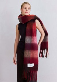 Écharpe à carreaux rouge et gris en tissu doux, avec des bords frangés et une étiquette indiquant "ARCTIC FOX" près du bas.