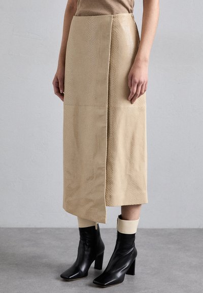 Gonna beige con motivo rettile e spacco laterale. Abbinata a stivaletti neri in pelle con una fascia crema alla caviglia.