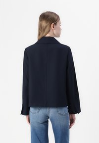 Marineblå cropped blazer lavet af et glat stof med en klapkrave og åbne ærmer, parret med lyseblå jeans.