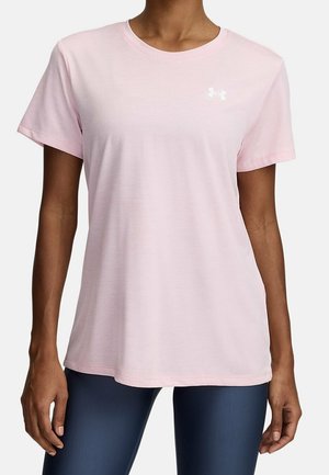 Vrouw draagt een lichtroze kortärmelig T-shirt met ronde hals en een klein wit Under Armour-logo op de borst, gecombineerd met donkerblauwe leggings.