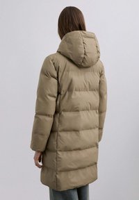 Parka acolchada en marrón claro con capucha. Presenta una silueta cuadrada y textura acolchada. Mangas largas y llega hasta la mitad del muslo.