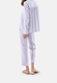 Camicia a righe viola chiaro con bottoni, schiena arricciata e polsini con rouches, abbinata a pantaloni viola chiaro e sandali piatti.