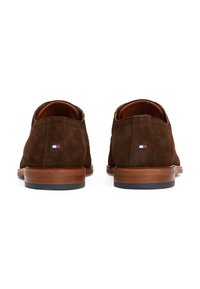 Chaussures en daim marron avec une texture lisse, bout rond et talon en bois empilé. Présente un petit patch logo à l'arrière près du talon.