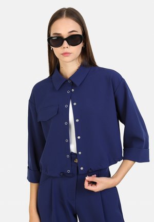 Veste cropped bleu marine avec une fermeture à boutons, col, poche poitrine et manches retroussées ; présente des détails de cordon de serrage au niveau de l'ourlet.
