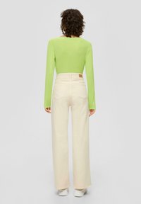 Groene lange mouwen top en crèmekleurige hoge taille wijde broek met achterzakken. Lichtgewicht stof en naadloos ontwerp. Witte sneakers maken de uitstraling compleet.