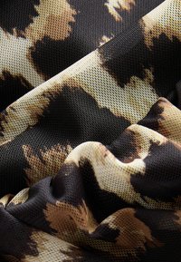 Tissu à imprimé animal présentant une texture en maille avec des motifs noirs, bruns et crèmes, mettant en valeur un tombé doux et un contraste de couleurs vibrantes.