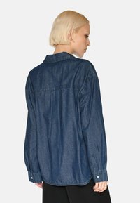 Camicia di jeans blu scuro con una vestibilità comoda, maniche lunghe, polsini con bottoni e colletto classico. Tessuto liscio con cuciture sottili.