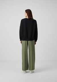Felpa nera con polsini e orlo a coste, abbinata a pantaloni ampi verde oliva. Tessuto morbido, vestibilità rilassata. Come calzature, scarpe da ginnastica bianche.