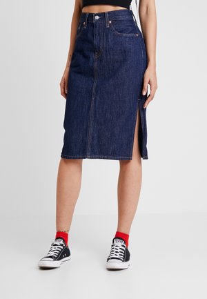 Falda midi de mezclilla azul oscuro con abertura frontal, combinada con calcetas rojas y zapatillas negras bajas, mostrada desde la cintura hasta los tobillos.