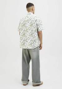 Kortærmet, skjorte med krave i hvid bundfarve, prydet med grønne og gule bladmønstre. Sammen med afslappede, lysegrå jeans.